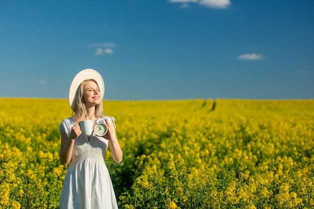 Mooie vrouw in jurk met kop koffie in koolzaad veld