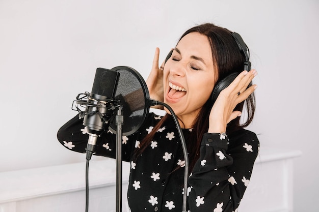 Mooie vrouw in koptelefoon zingt een lied in de buurt van een microfoon in een opnamestudio