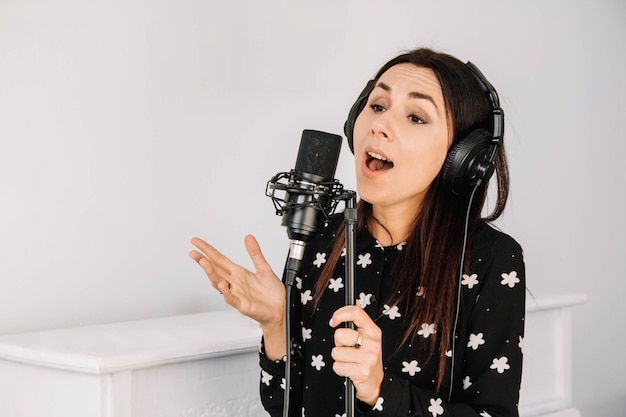 Mooie vrouw in koptelefoon zingt een lied in de buurt van een microfoon in een opnamestudio