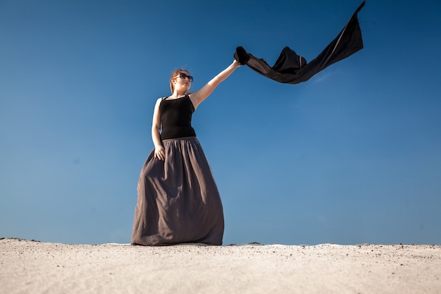 Mooie vrouw in lange jurk met zwarte doek staande op zandduin
