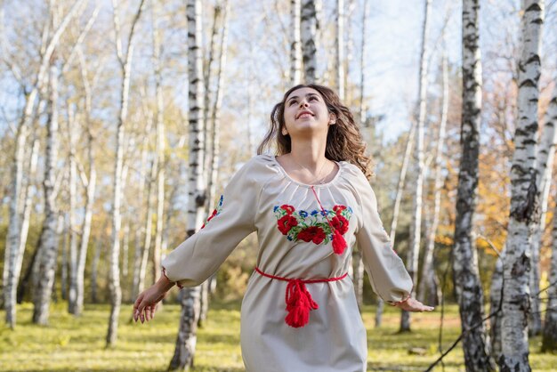 Mooie vrouw in Oekraïense nationale traditionele kostuumkleren die in bos dansen