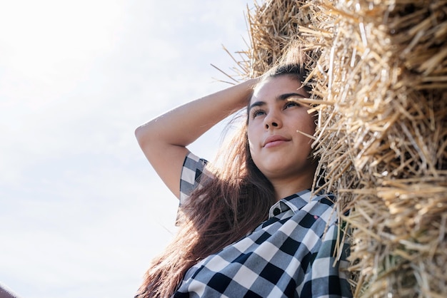 Mooie vrouw in plaidoverhemd en cowboyhoed die op hooiberg rusten