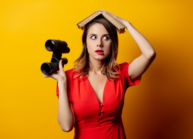 Mooie vrouw in rode jurk met boek en verrekijker