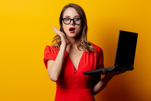 Mooie vrouw in rode jurk met laptopcomputer op gele muur