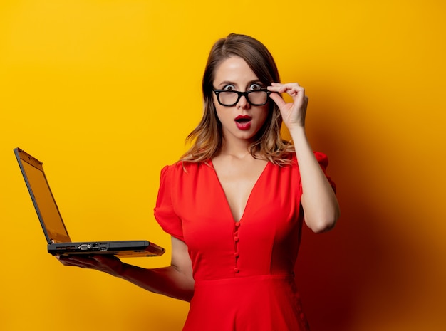 Mooie vrouw in rode jurk met laptopcomputer op gele muur