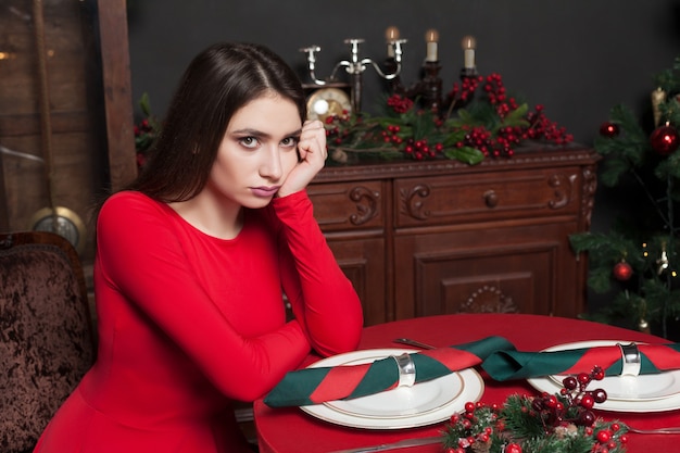 Mooie vrouw in rode jurk te wachten aan de tafel in restaurant met rijk interieur.