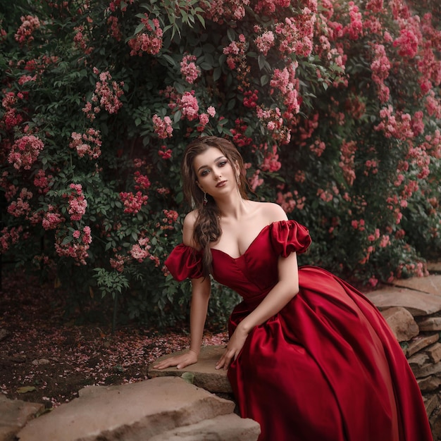 Mooie vrouw in rode jurk wandelen in de tuin vol rozen.