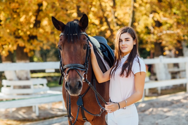 mooie vrouw in speciale uniforme professionele paardentrainer die bij bruin paard blijft en glimlacht