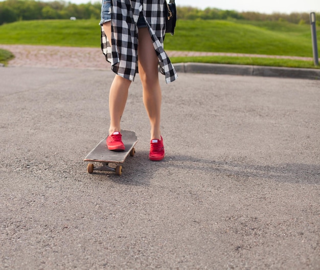 Mooie vrouw in spijkerbroek schaatst op het asfalt in roze schoenen op de achtergrond