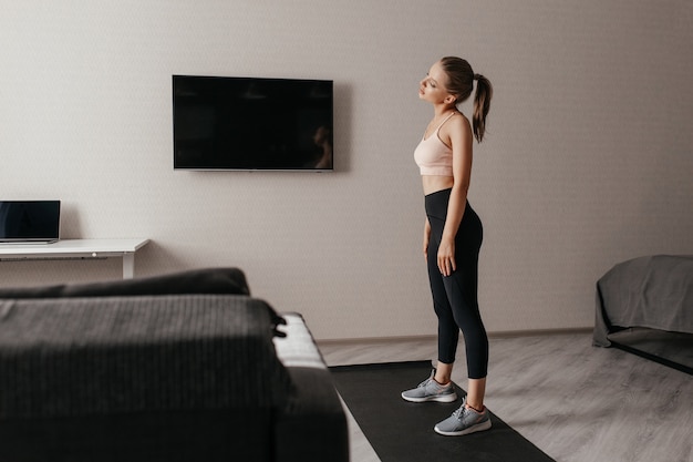 Mooie vrouw in sportkleding die thuis opwarmen alvorens met training te beginnen