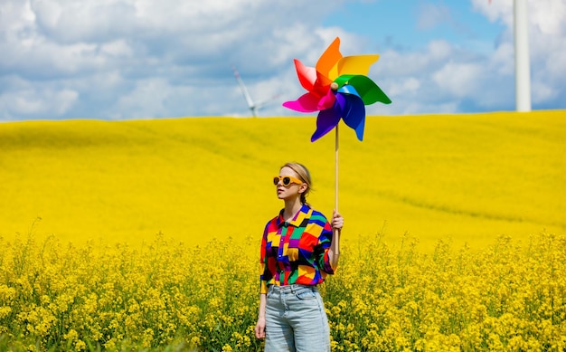 Mooie vrouw in stijlvol shirt uit de jaren 90 met pinwheel in koolzaadveld