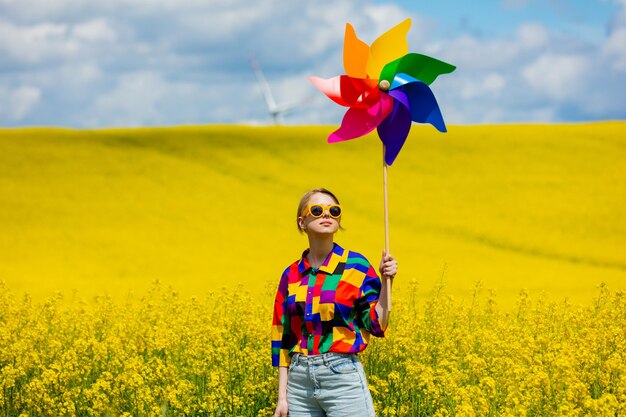 Mooie vrouw in stijlvol shirt uit de jaren 90 met pinwheel in koolzaadveld