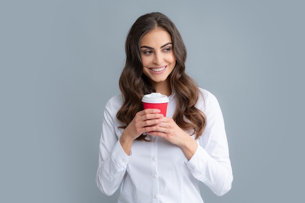 Mooie vrouw in studio met kopje koffie Foto van vrolijke positieve mooie girlf met mok koffie glimlachend tandenpoetsend geïsoleerd over grijze achtergrond