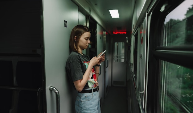 Mooie vrouw in vrijetijdskleding die in de treingang staat met een smartphone in haar handen