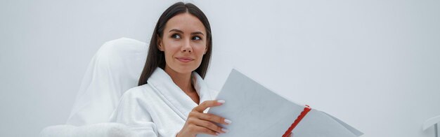 Mooie vrouw in witte badjas die een tijdschrift leest terwijl ze in een luxe wellness-spa zit
