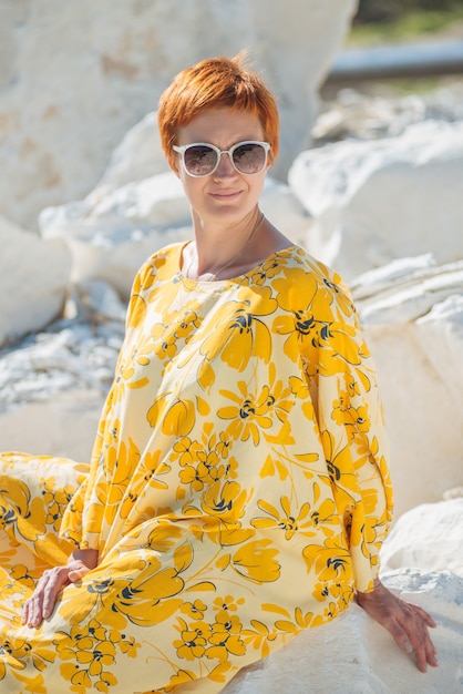 Mooie vrouw in zonnebril in gele jurk in het zand van zeer warm weer