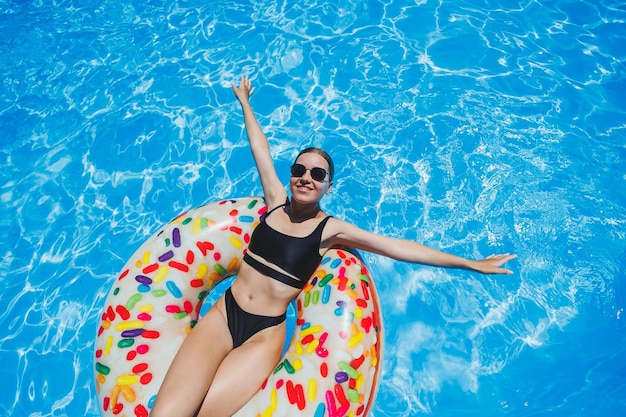 Mooie vrouw in zonnebril in het zwembad drijft op een opblaasbare zwemring in een zwarte zwembroek zomerfoto zwemmen fotografie zomer vrouw foto's