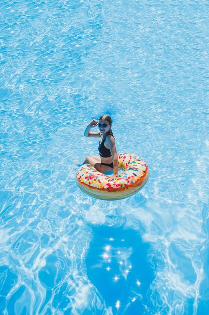 Mooie vrouw in zonnebril in het zwembad drijft op een opblaasbare zwemring in een zwarte zwembroek zomerfoto zwemmen fotografie zomer vrouw foto's