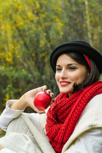 Mooie vrouw in zwarte hoed en rode sjaal met een rode appel in haar hand. Herfst picknick buiten