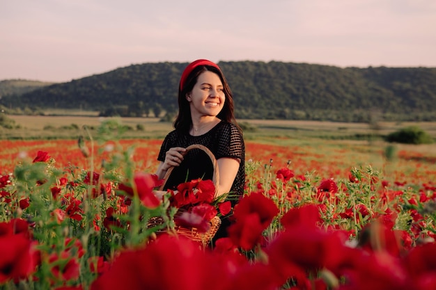 Mooie vrouw in zwarte jurk bij zonsondergang op het veld met papaversbloemen