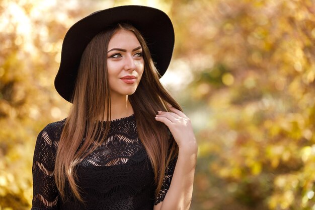 Mooie vrouw in zwarte jurk en hoed in de herfst