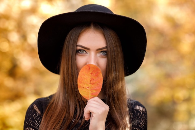 Mooie vrouw in zwarte jurk en hoed in de herfst