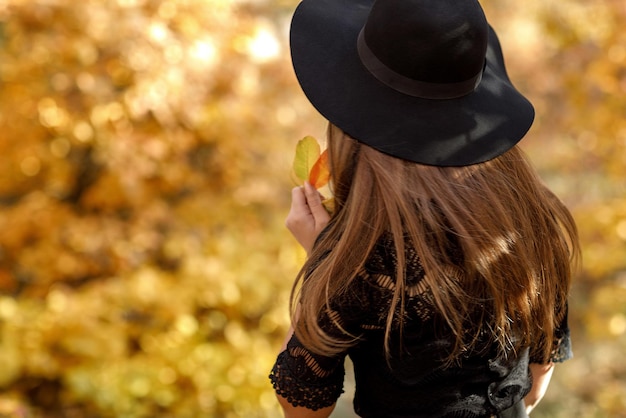 Mooie vrouw in zwarte jurk en hoed in de herfst