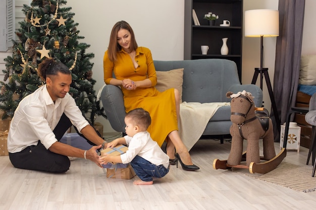 Mooie vrouw, jonge mulatman en een peuterkind sorteren vrolijk dozen met geschenken in de buurt van een