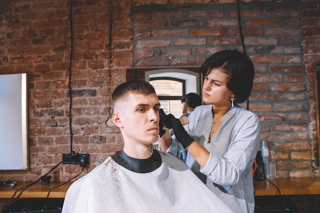 Mooie vrouw Kapper scheert het hoofd van de klant met een elektrische trimmer in kapperszaak. Reclame en kapperszaak concept