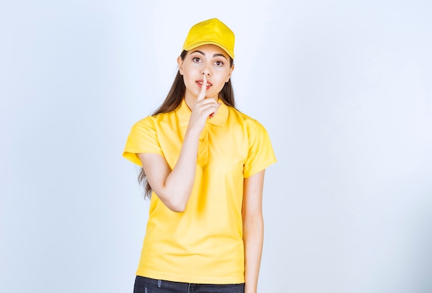 Mooie vrouw koerier in gele uniform staan en poseren over witte muur.