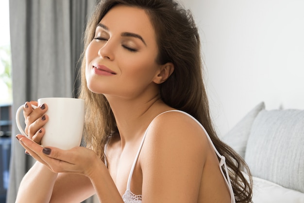 Mooie vrouw koffie of thee drinken in de slaapkamer