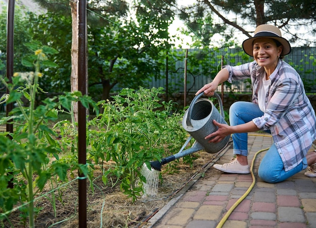 Mooie vrouw landbouwer die zorgt voor geplante zaailingen die planten water geven in de biologische boerderij landbouwhobby