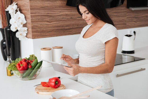 Mooie vrouw leest recept van tabletcomputer in de keuken