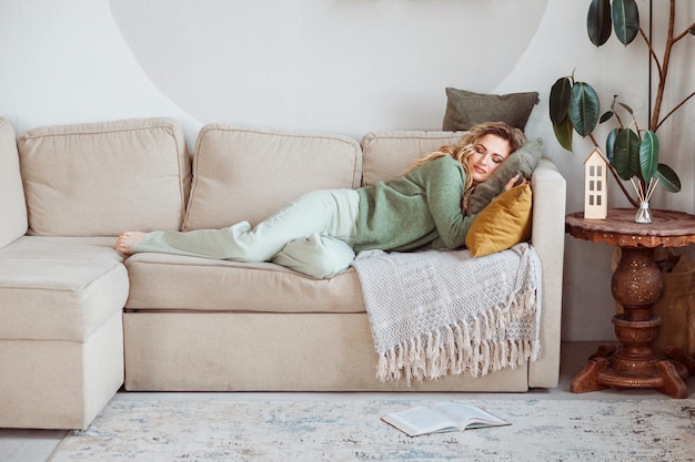 Mooie vrouw ligt thuis op de bank en slaapt open boek op het tapijt naast haar