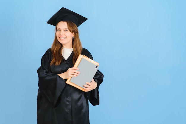 Mooie vrouw met afstuderen glb en ceremonie gewaad houden graad op zoek positief en gelukkig staan en glimlachen met een zelfverzekerde glimlach