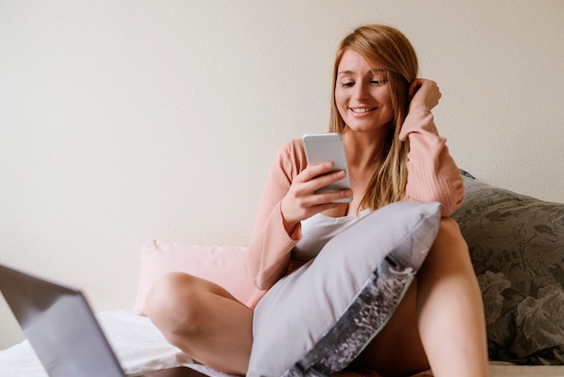 Mooie vrouw met behulp van de mobiel en laptop in de slaapkamer.