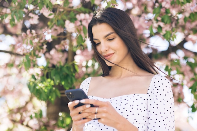 mooie vrouw met behulp van een smartphone in het park op een achtergrond van sakura bomen