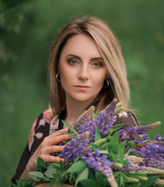 Mooie vrouw met blond haar in een jurk in de natuur met bloemen in haar handen