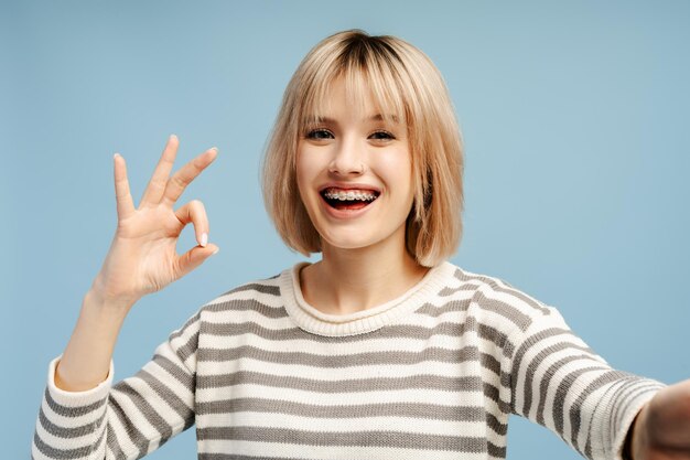 Mooie vrouw met blond haar met beugels die selfie maakt en naar de camera kijkt.