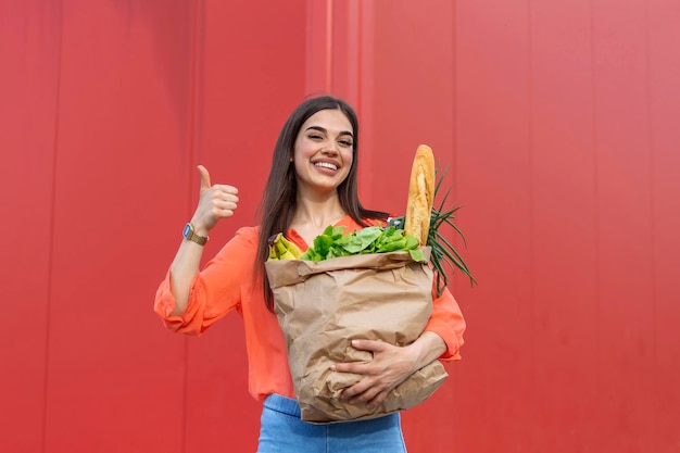 Mooie vrouw met boodschappentassen op rode achtergrond met duimen omhoog Gelukkig mooi meisje met tas met boodschappen op rode achtergrond