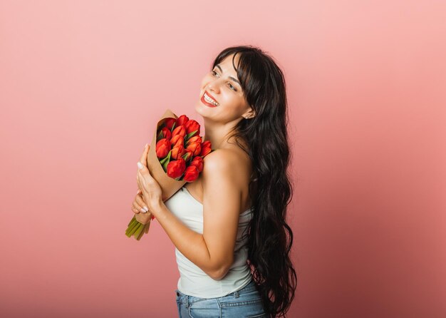 Mooie vrouw met een boeket van lentebloem tulpen op een roze achtergrond Gift womens day concept