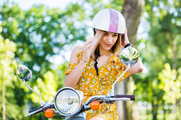 Mooie vrouw met een gele jurk op een scooter