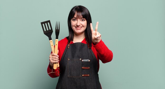 Mooie vrouw met een grote maat die lacht en er gelukkig, zorgeloos en positief uitziet, gebarend naar overwinning of vrede met één hand