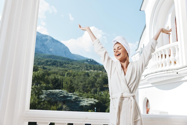 Mooie vrouw met een handdoek op mijn hoofd in een witte badjas die op het balkon verblijft in een hotel Mountain View Foto van hoge kwaliteit