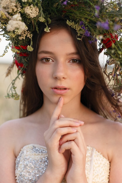 Mooie vrouw met een krans op haar hoofd zittend in een veld in bloemen.