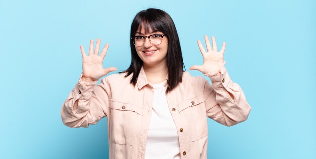 Mooie vrouw met een maatje meer die lacht en er vriendelijk uitziet, nummer tien of tiende toont met de hand naar voren, aftellend