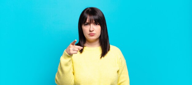 Mooie vrouw met een maatje meer die naar de camera wijst met een boze agressieve uitdrukking die eruitziet als een woedende, gekke baas