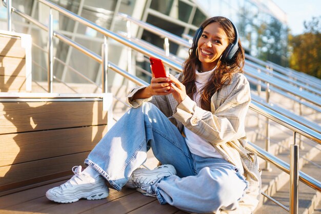 Mooie vrouw met een mobiele telefoon in de stad terwijl ze muziek luistert via oortjes Muziek emoties