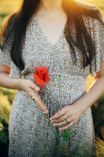 Mooie vrouw met een papaverbloem in het zonsondergangslicht in een gerstveld Atmosfeer rustig moment rustiek langzaam leven Stijlvol vrouwelijk wildbloemen verzamelen en genieten van de avond zomer landschap