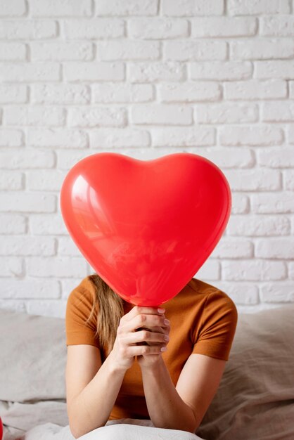 Mooie vrouw met een rode hartvormige ballon die in bed zit